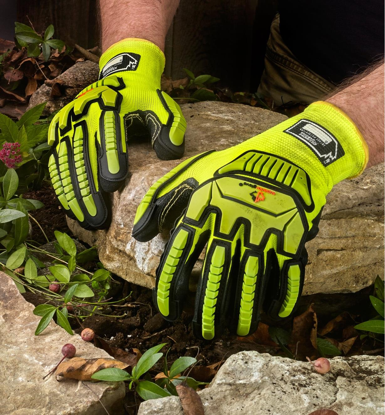 A landscaper wears impact-resistant gloves while positioning a large rock in a garden