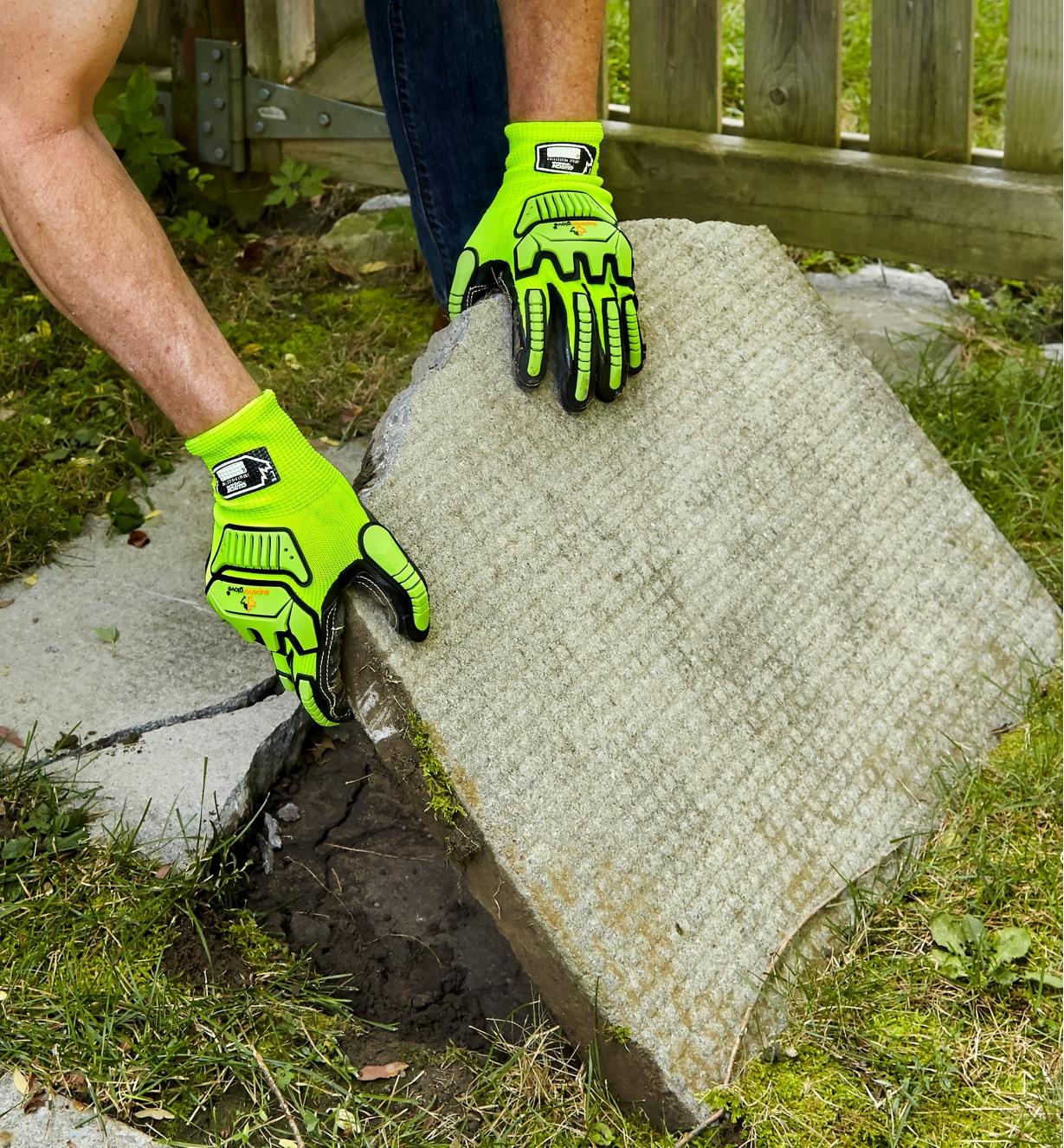 A landscaper wears impact-resistant gloves while removing an old, cracked patio stone