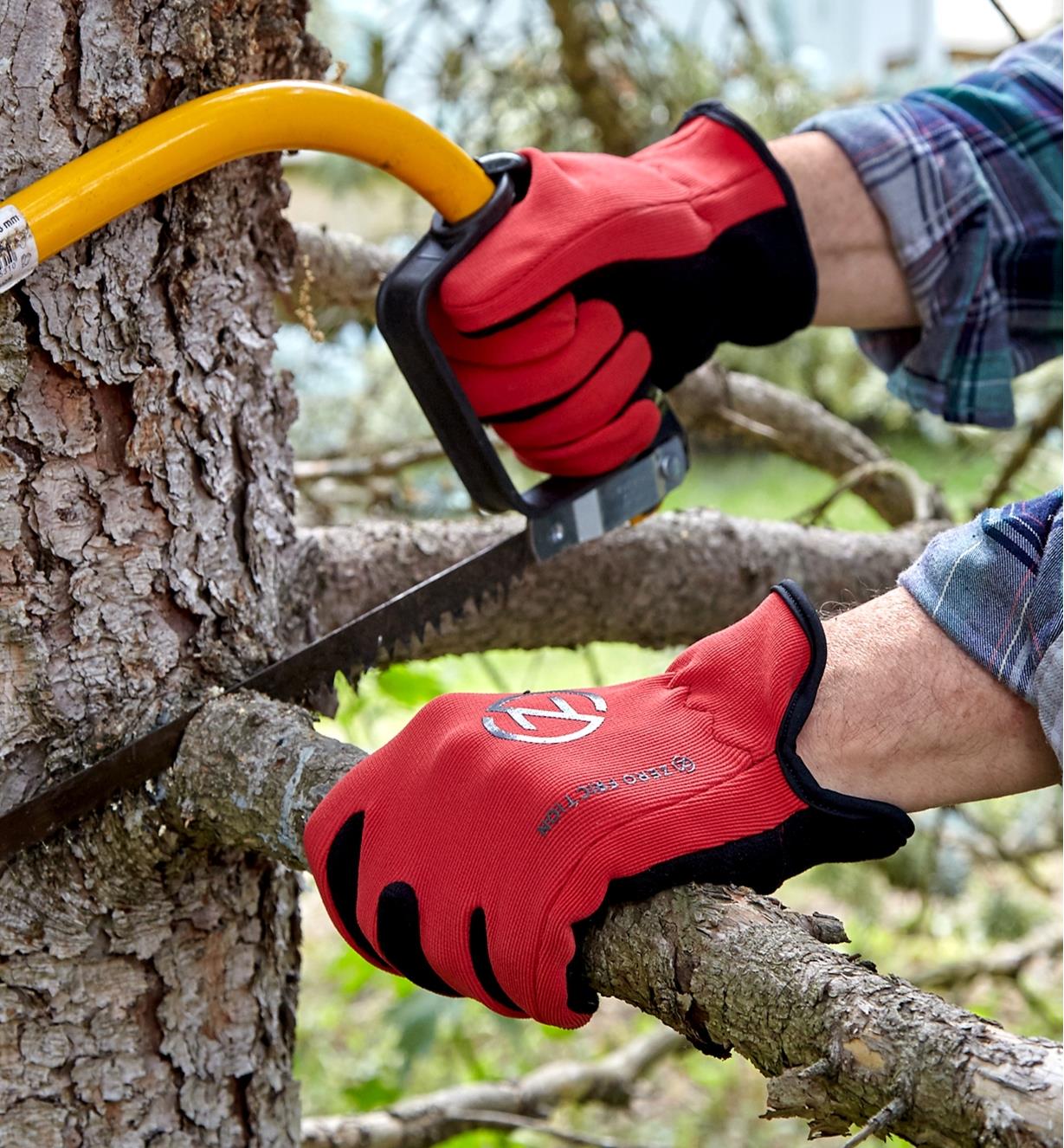 A person wears a pair of Universal-Fit gloves while using a bow saw to cut a limb from a tree