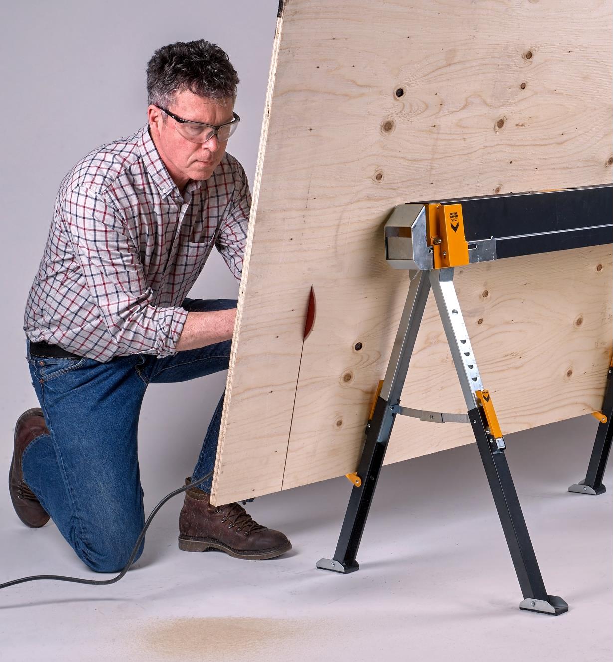 Using a circular saw to cut a plywood sheet held vertically on the lower brackets of a C700 sawhorse