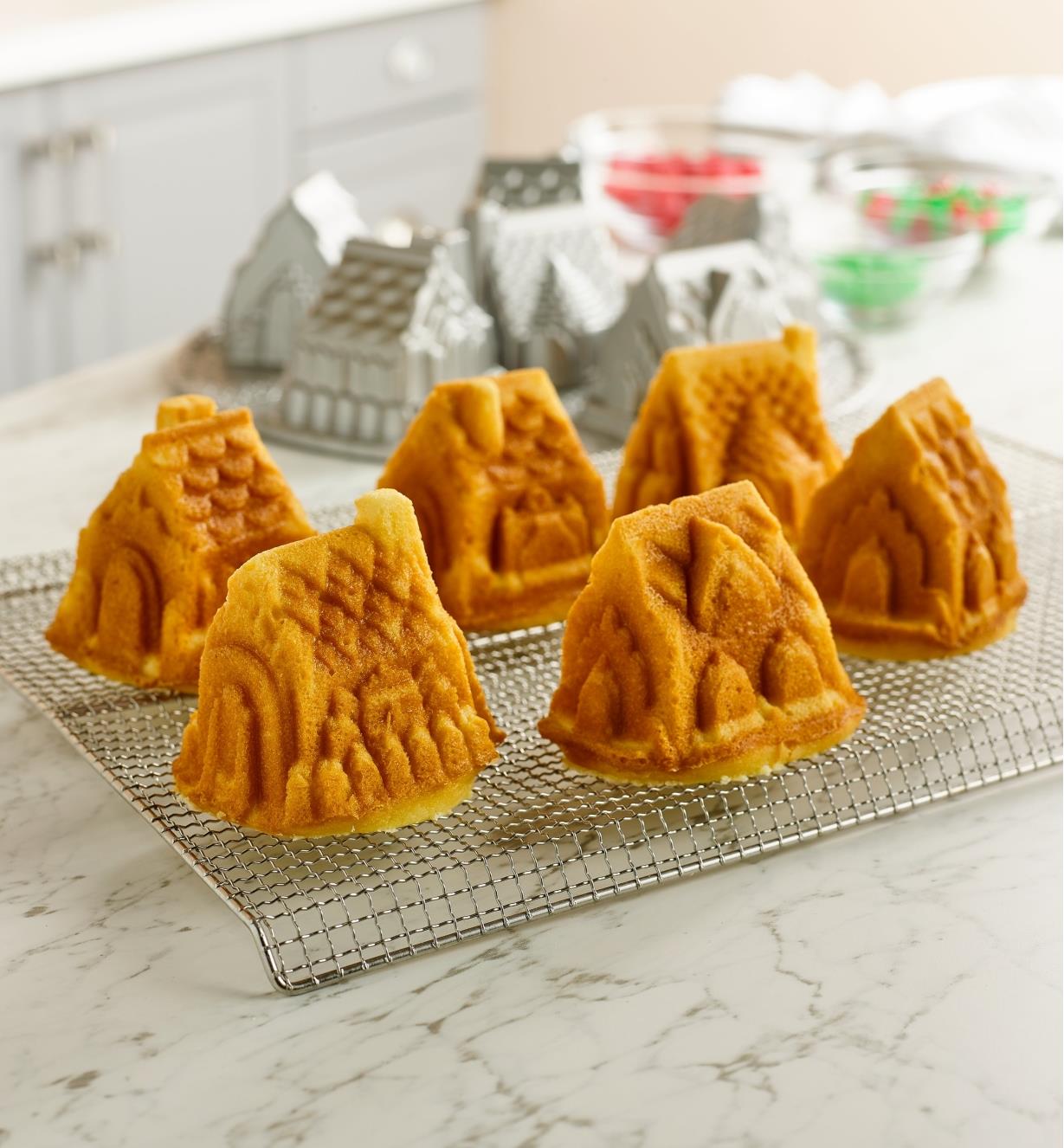 Six house-shaped cakes on a cooling rack, with the cozy village pan in the background