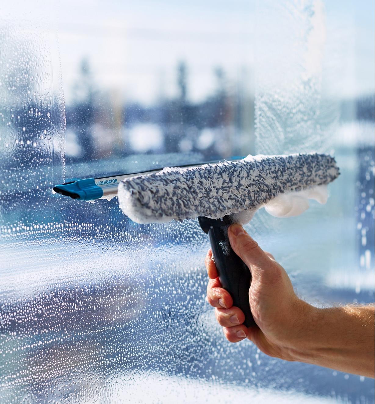 Using the squeegee side of the tool to clear soapy water from a window