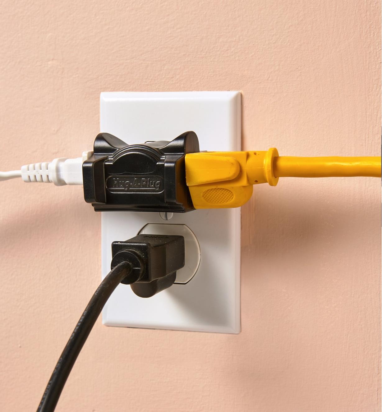 Black Hug-A-Plug adapter, with two plugs attached, plugged into a wall outlet 