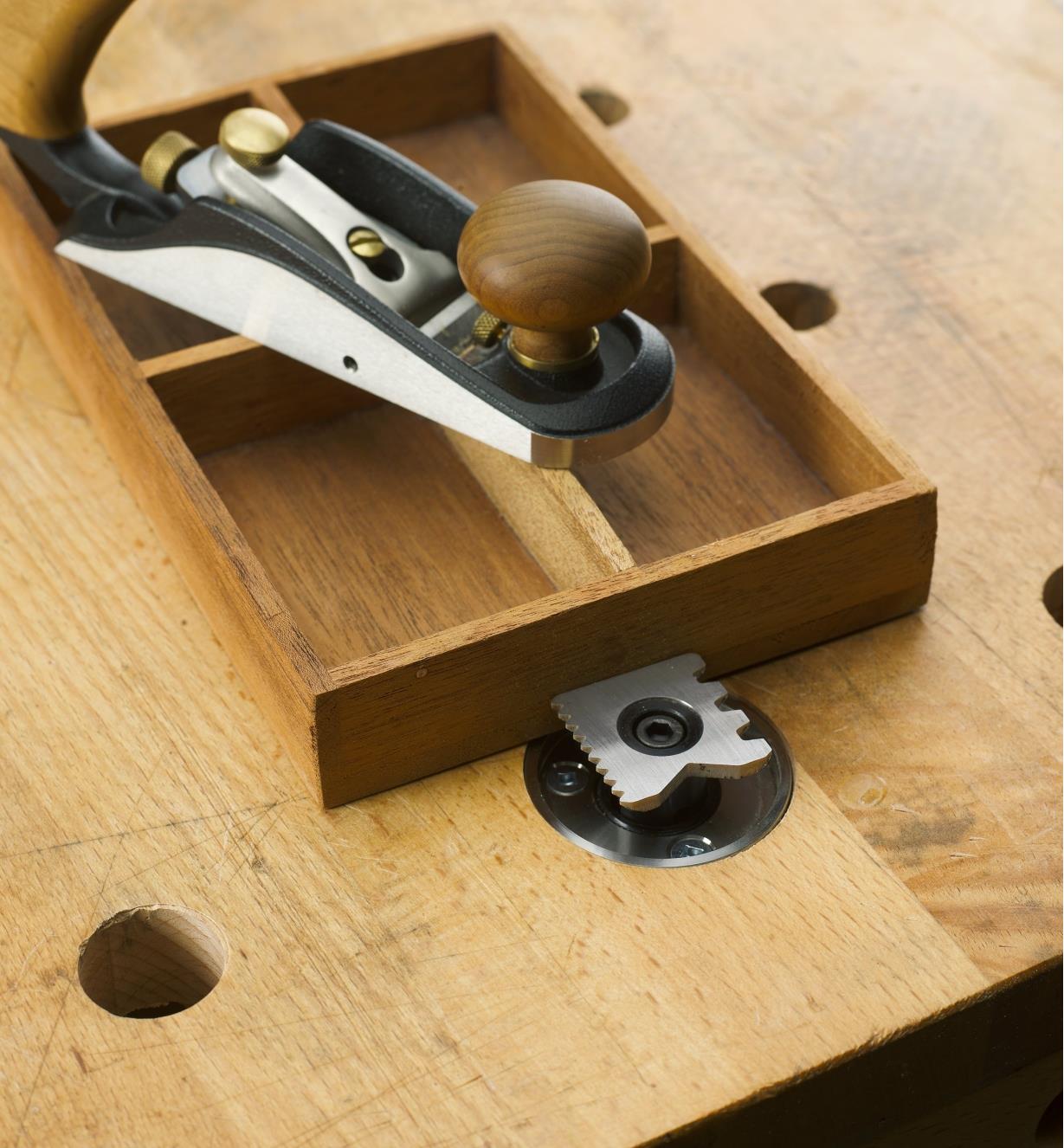 A plane rests of a wooden box held against the bench stop on a workbench