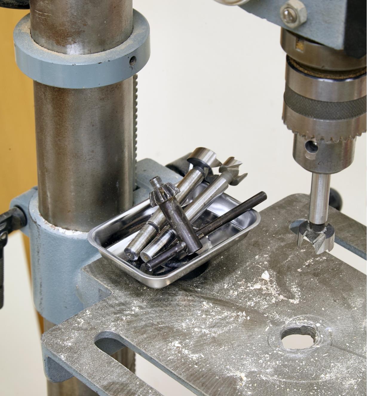 Mèches et clé de mandrin déposées dans un petit plateau magnétique sur la table d'une perceuse à colonne