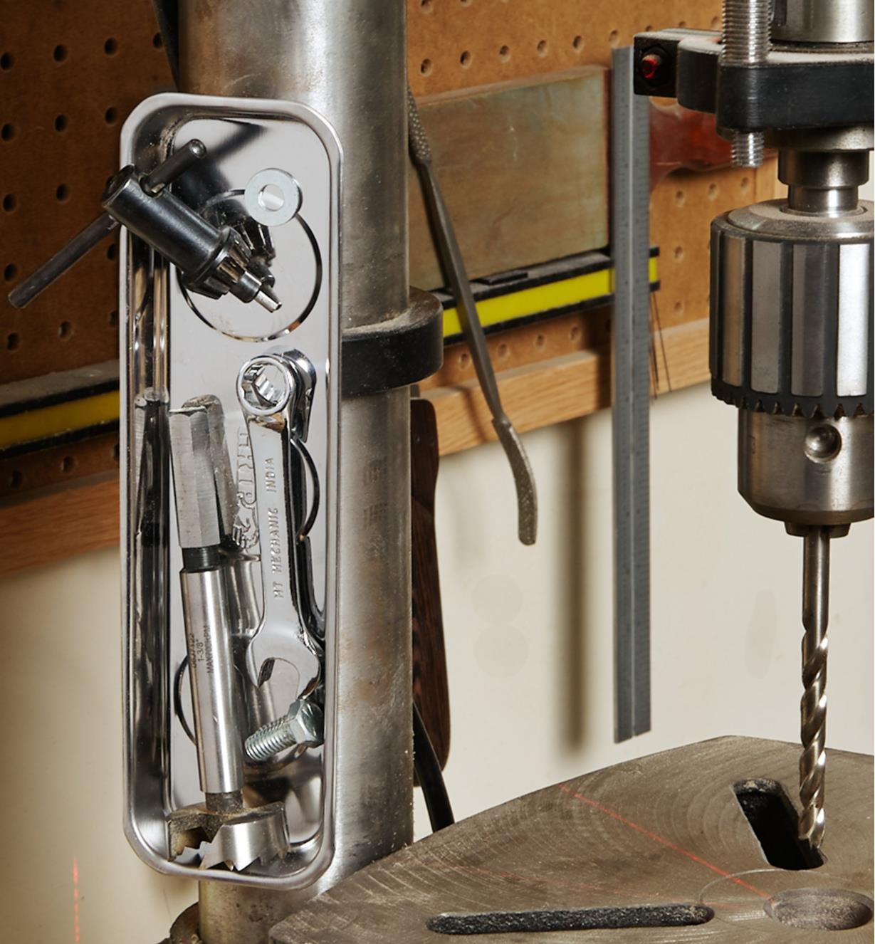 A magnetic parts tray filled with small items is held vertically against a metal column