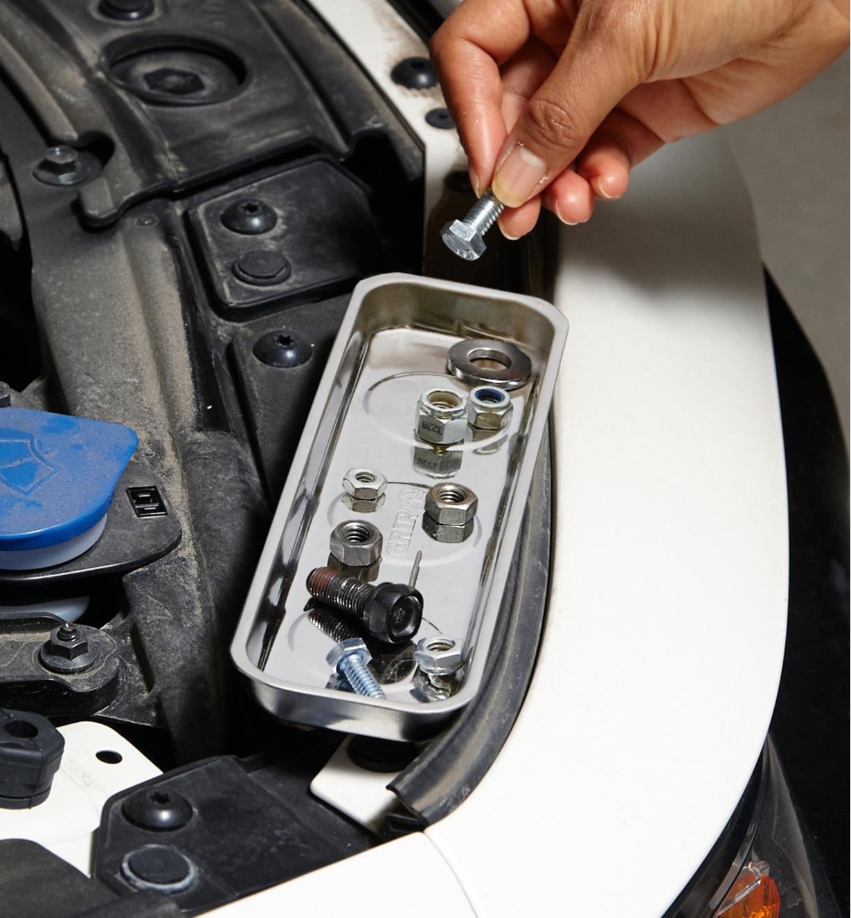 A magnetic parts tray is held against metal surfaces under a vehicle hood