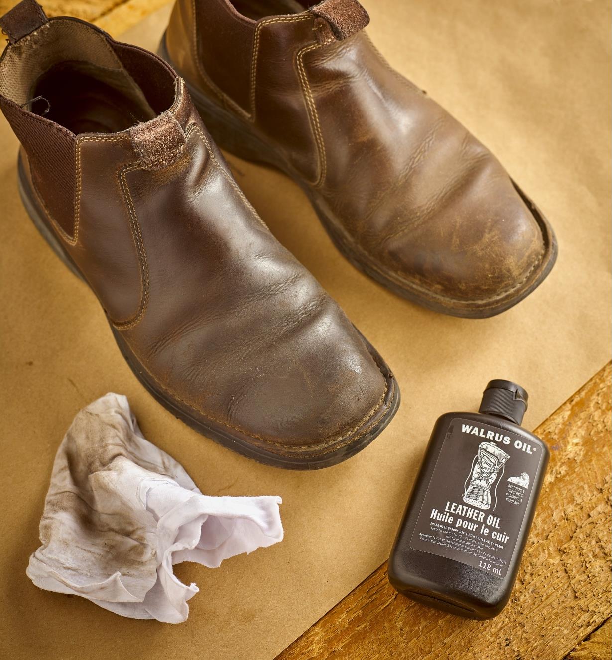 Paire de chaussures en cuir dont l'une a été enduite d'huile pour le cuir Walrus Oil près d'une bouteille d'huile et d'un chiffon