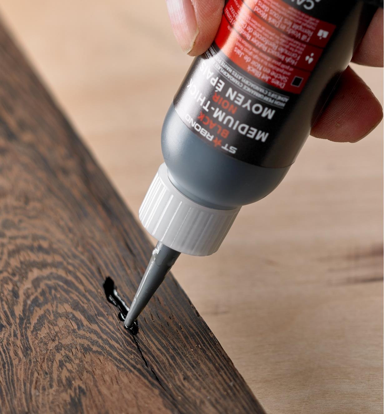 Applying Starbond black CA glue to a crack in a dark wood surface