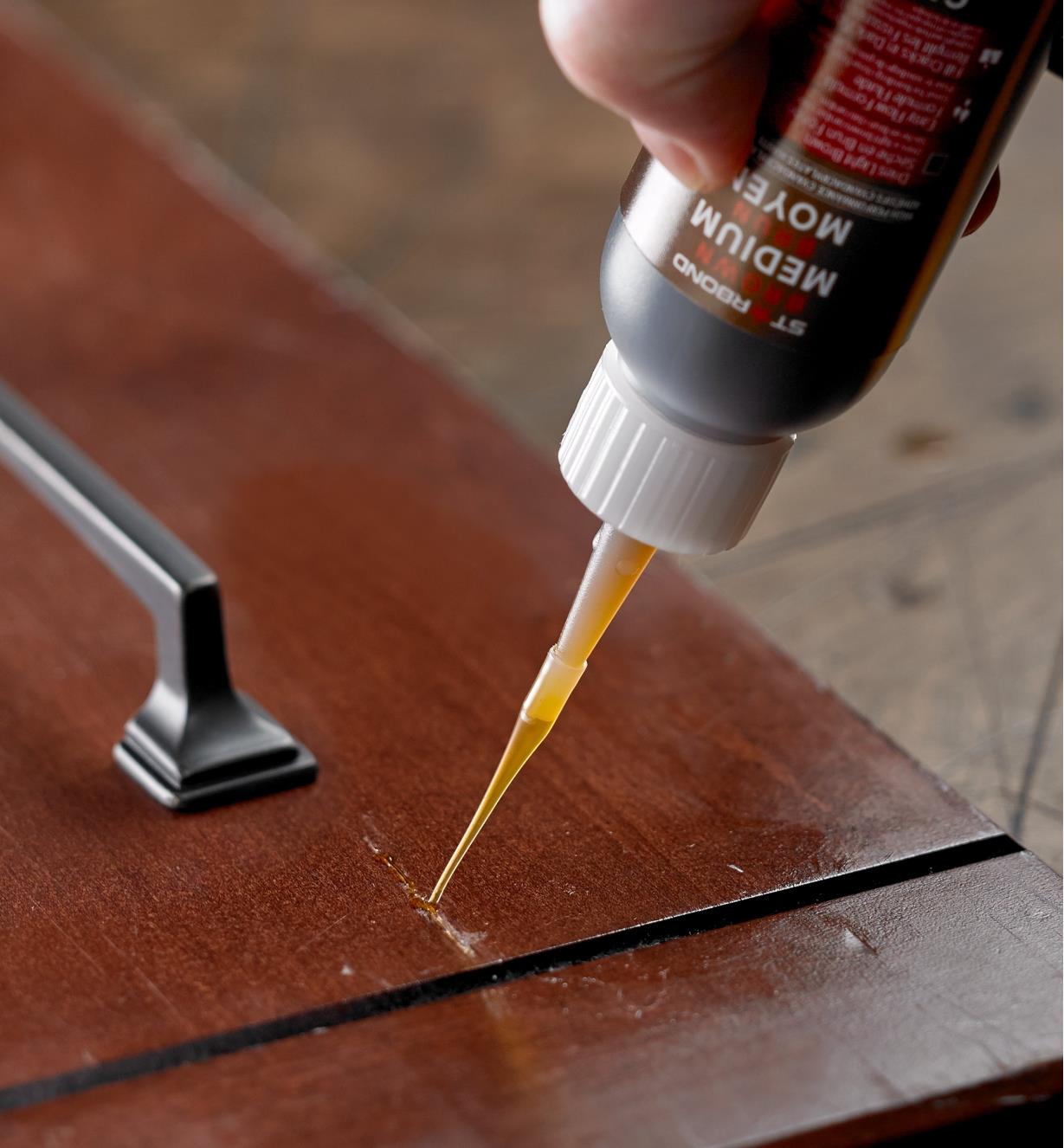 Applying Starbond brown CA glue to a crack in a wood surface