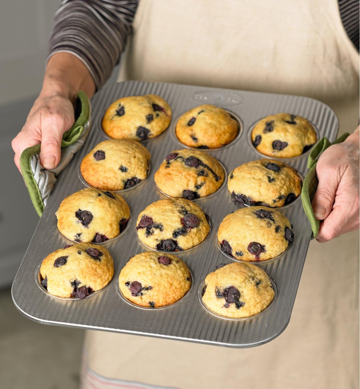 A baker holds a pan of a dozen blueberry muffins baked in a muffin pan made by USA Pan