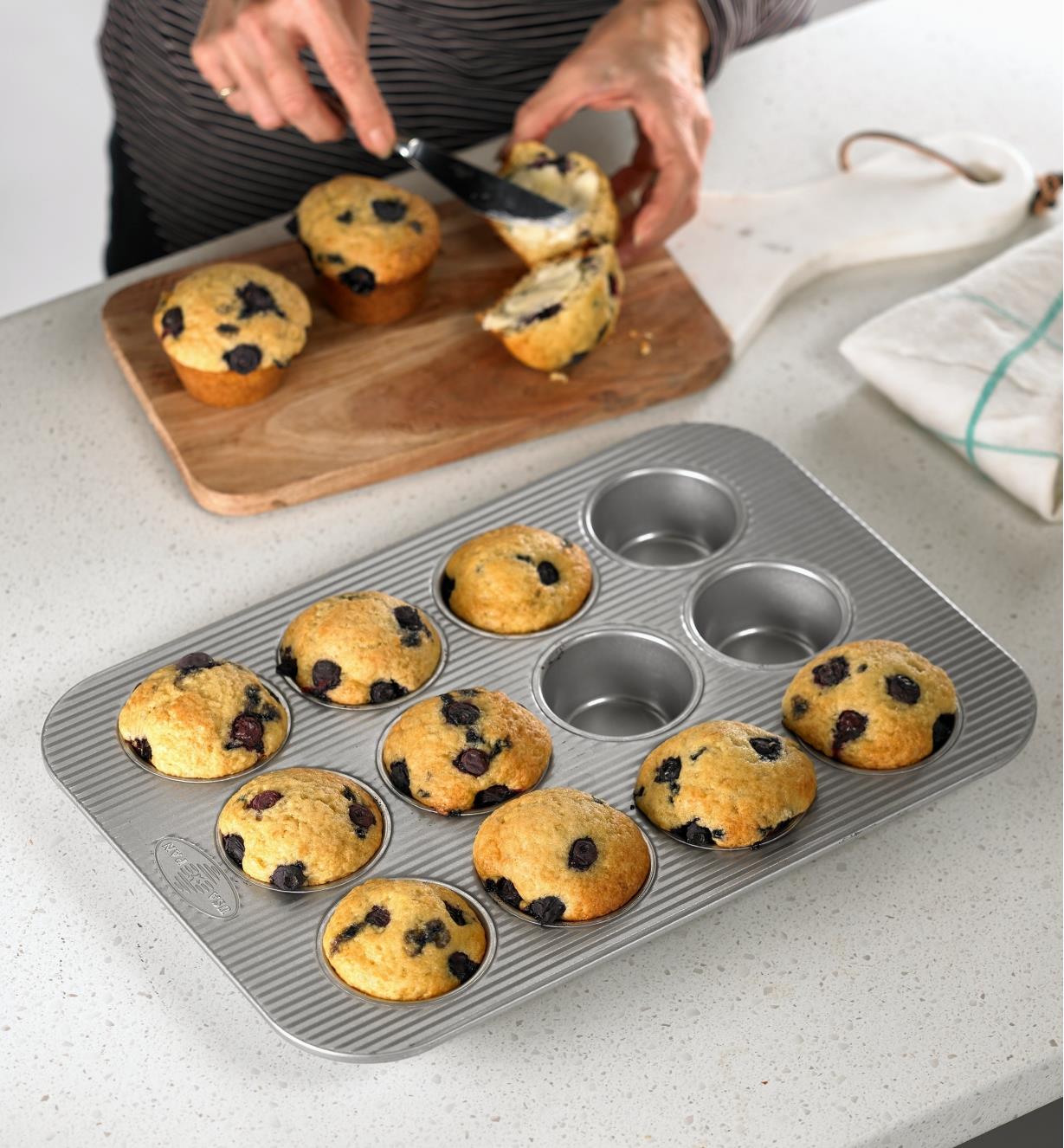 A woman butters one of twelve fresh blueberry muffins baked in a muffin pan made by USA Pan