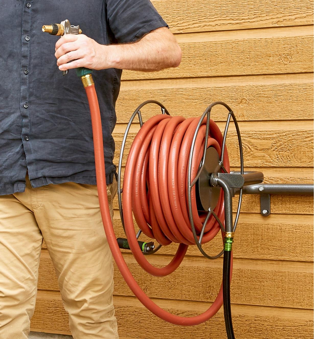 A man holds a sprayer attached to a hose held on a Wall-Mount Swivel Hose Reel
