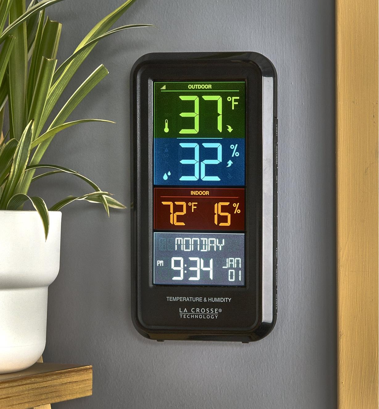 An indoor/outdoor weather station mounted on an interior wall, displaying various readings