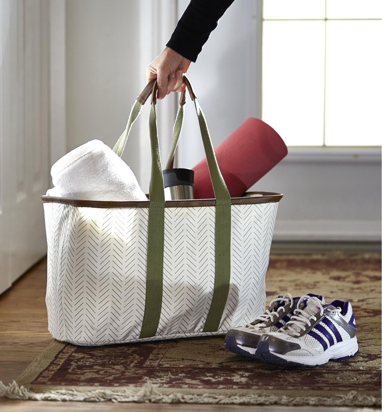 A person picks up a foldaway tote holding a yoga mat, towel and travel mug before leaving the house