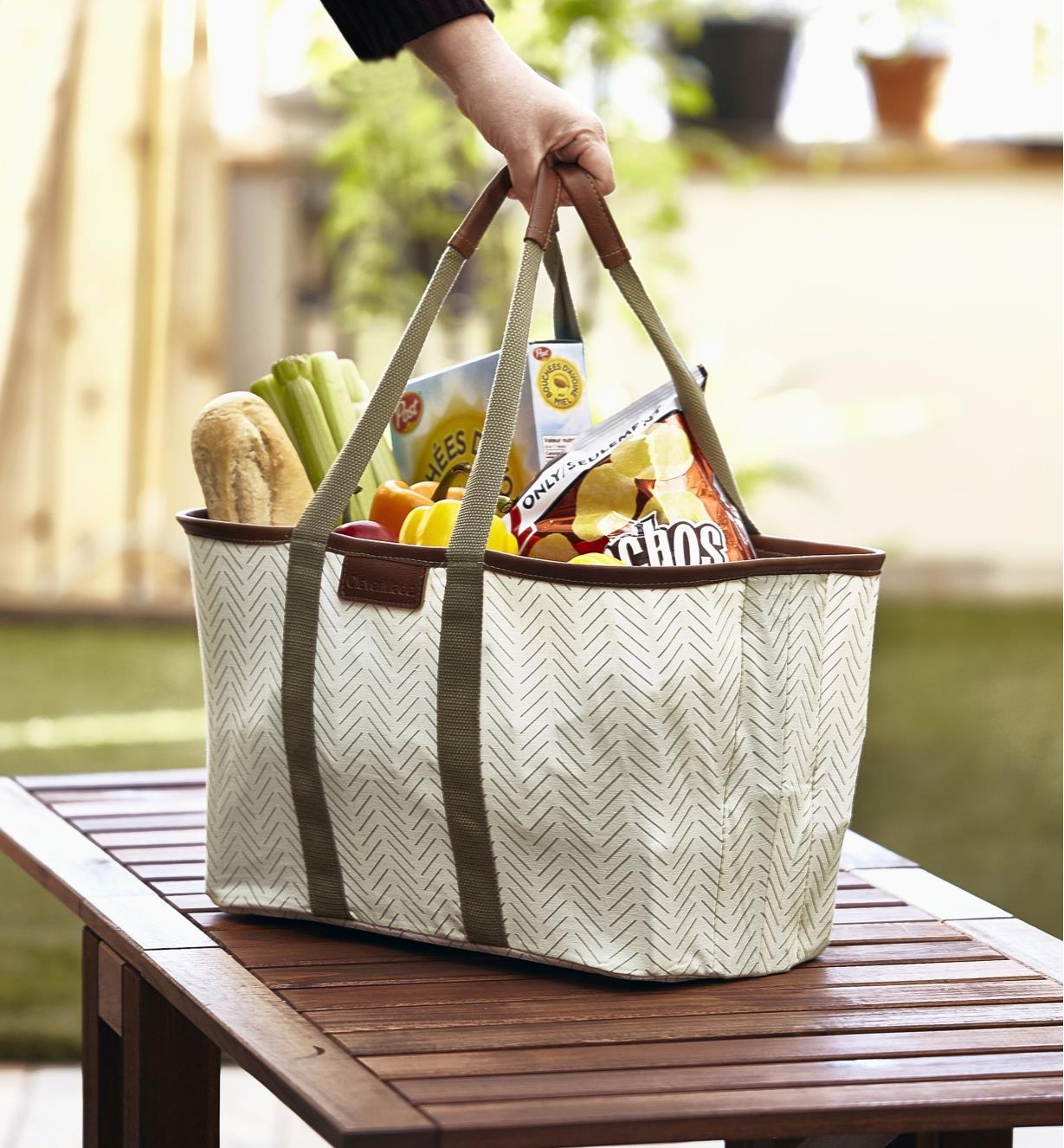 A person sets down a foldaway tote full of groceries on an outdoor table