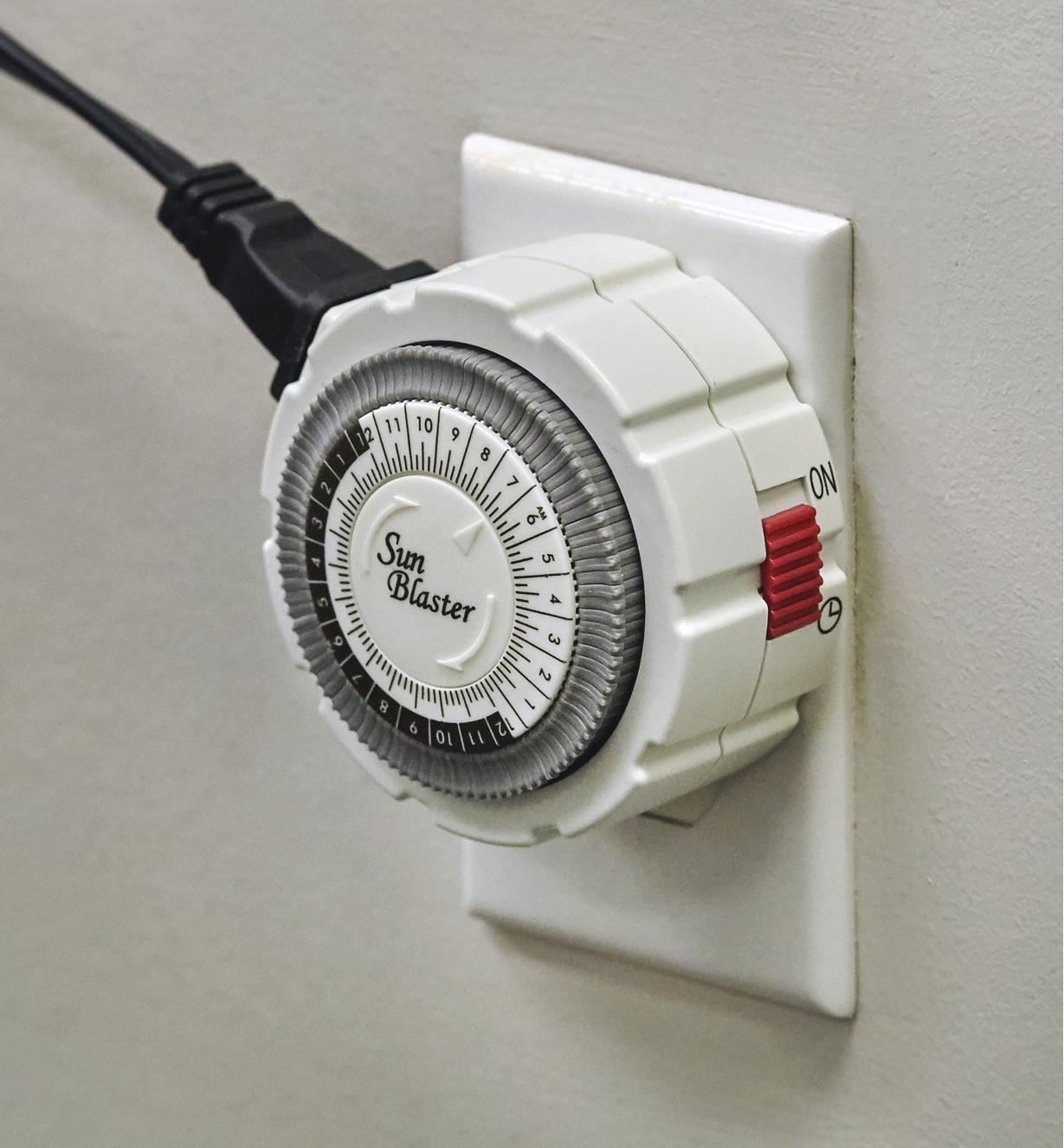 A close view of the mechanical timer connected to the grow-light cord and plugged into a wall outlet