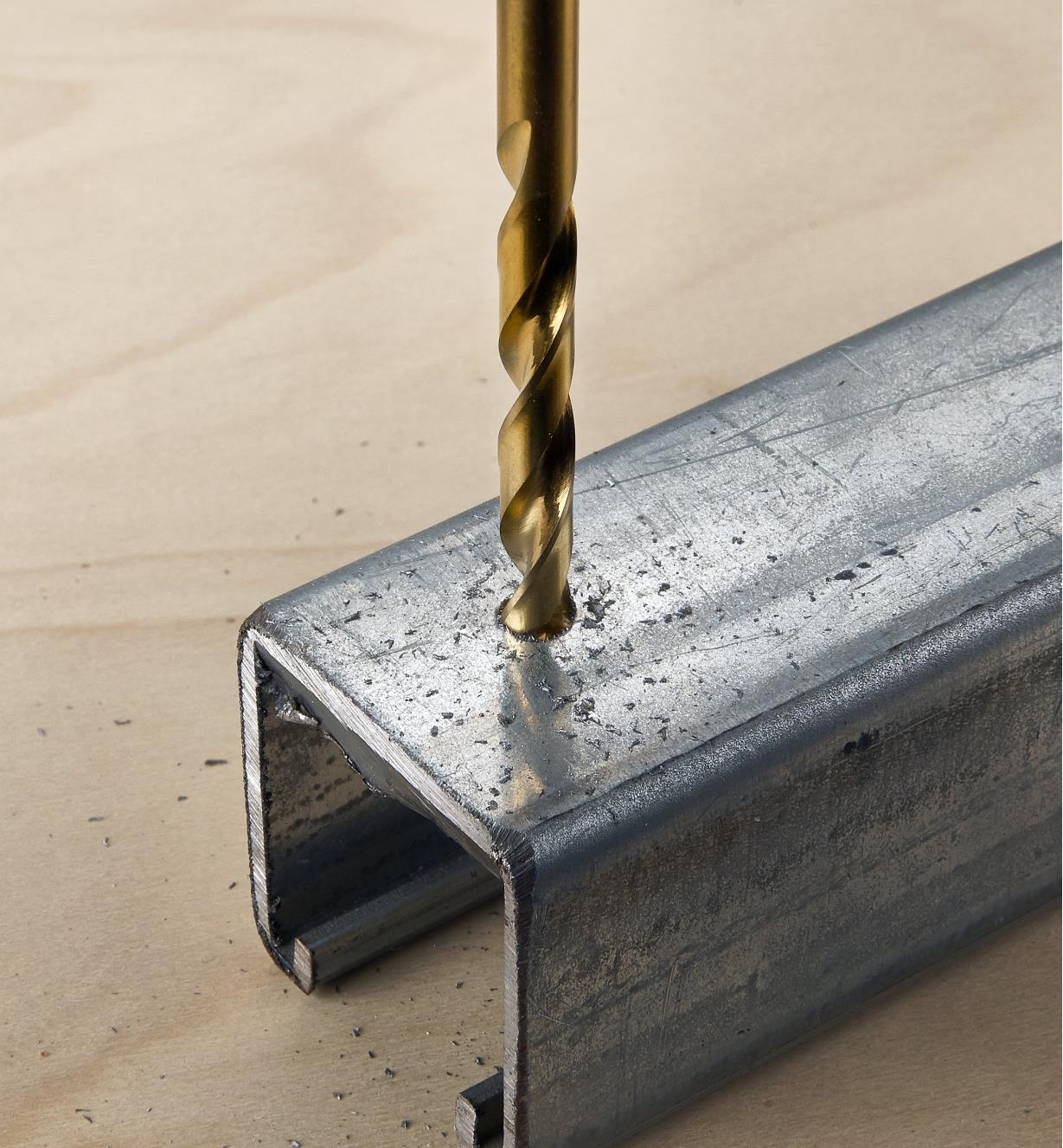 A close view of a hex-shank twist drill bit being used to drill a hole in a piece of steel U-channel