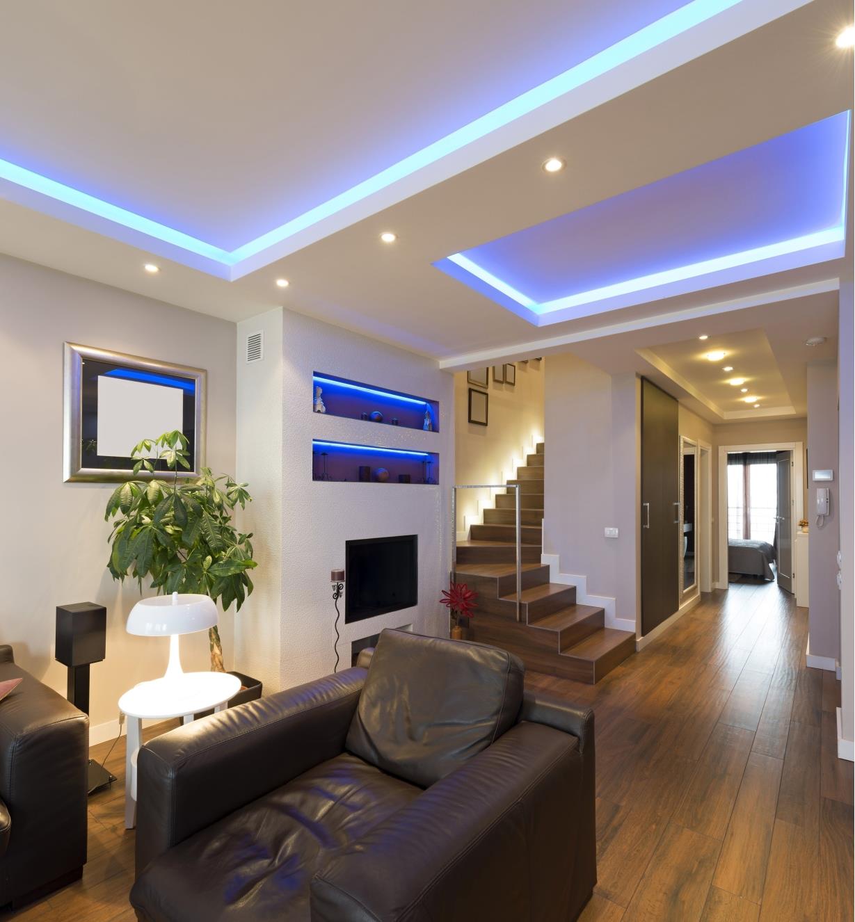 A room and hallway with glowing lights illuminating shelves, recessed ceilings, and a stairway