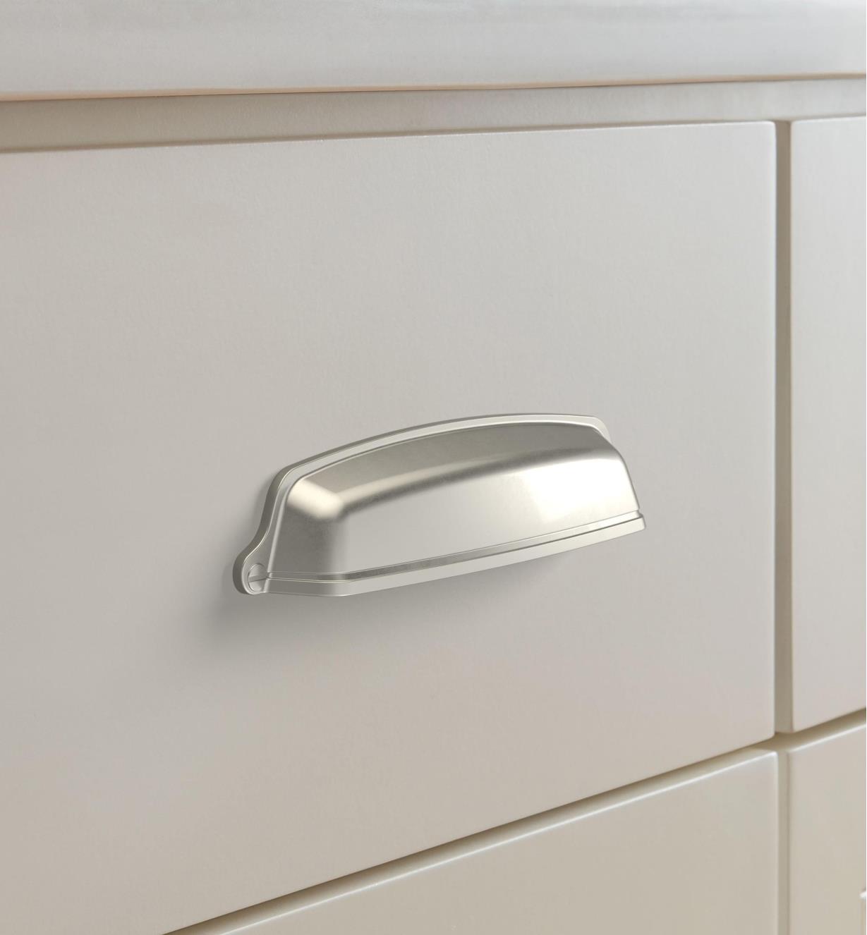 A satin nickel colored cup pull mounted horizontally on a drawer