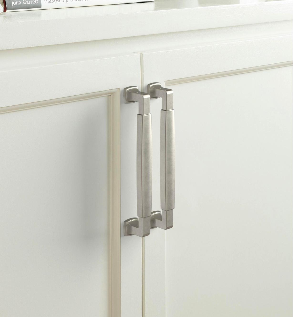 Two satin nickel colored Stature handles are connected vertically to two white colored cupboard doors