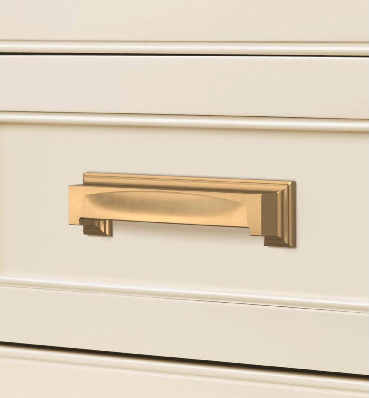 A champagne bronze Appoint cup pull connected horizontally to a white drawer