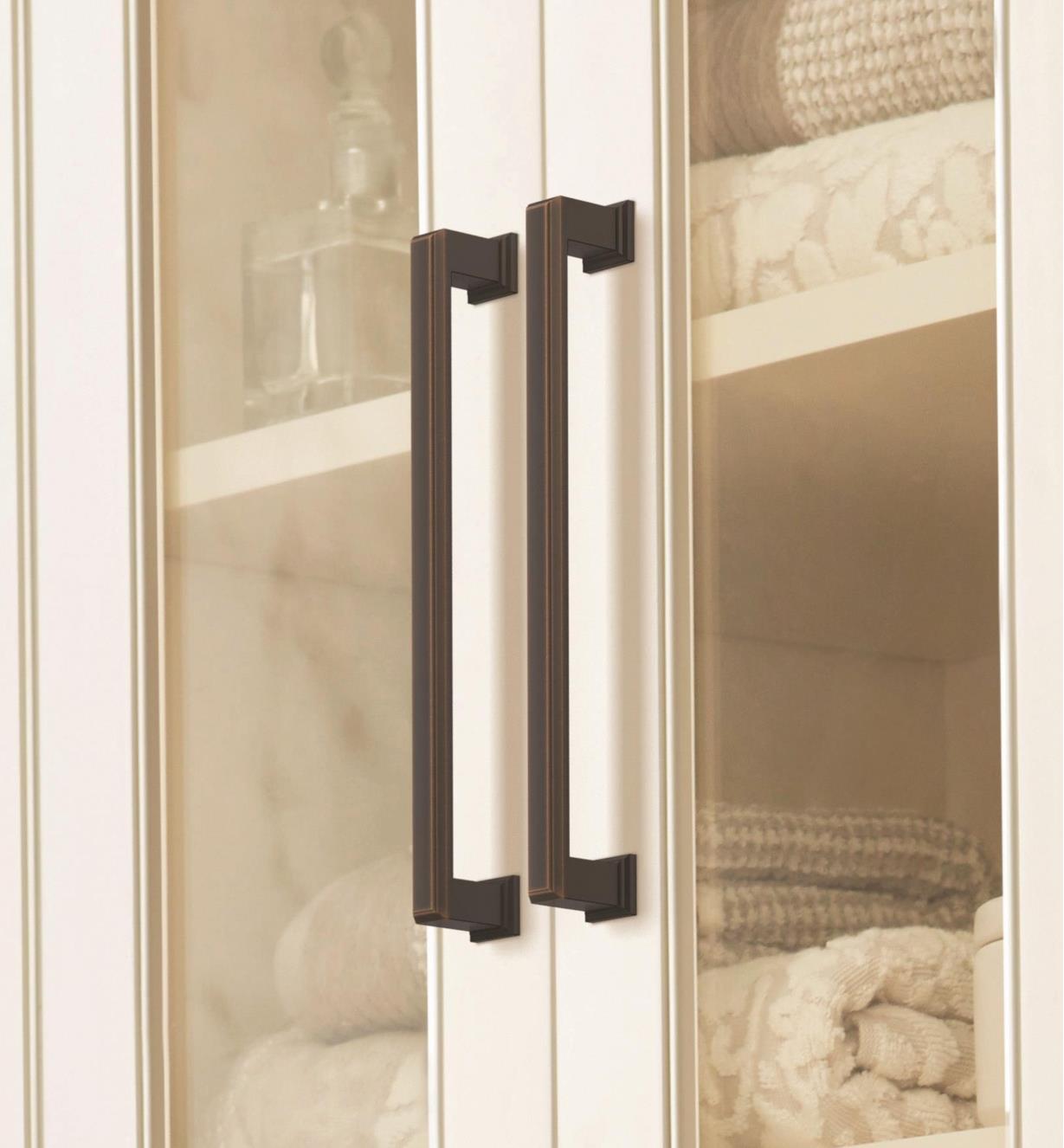 Two oil-rubbed bronze Appoint handles connected vertically to two cupboard doors with glass centers