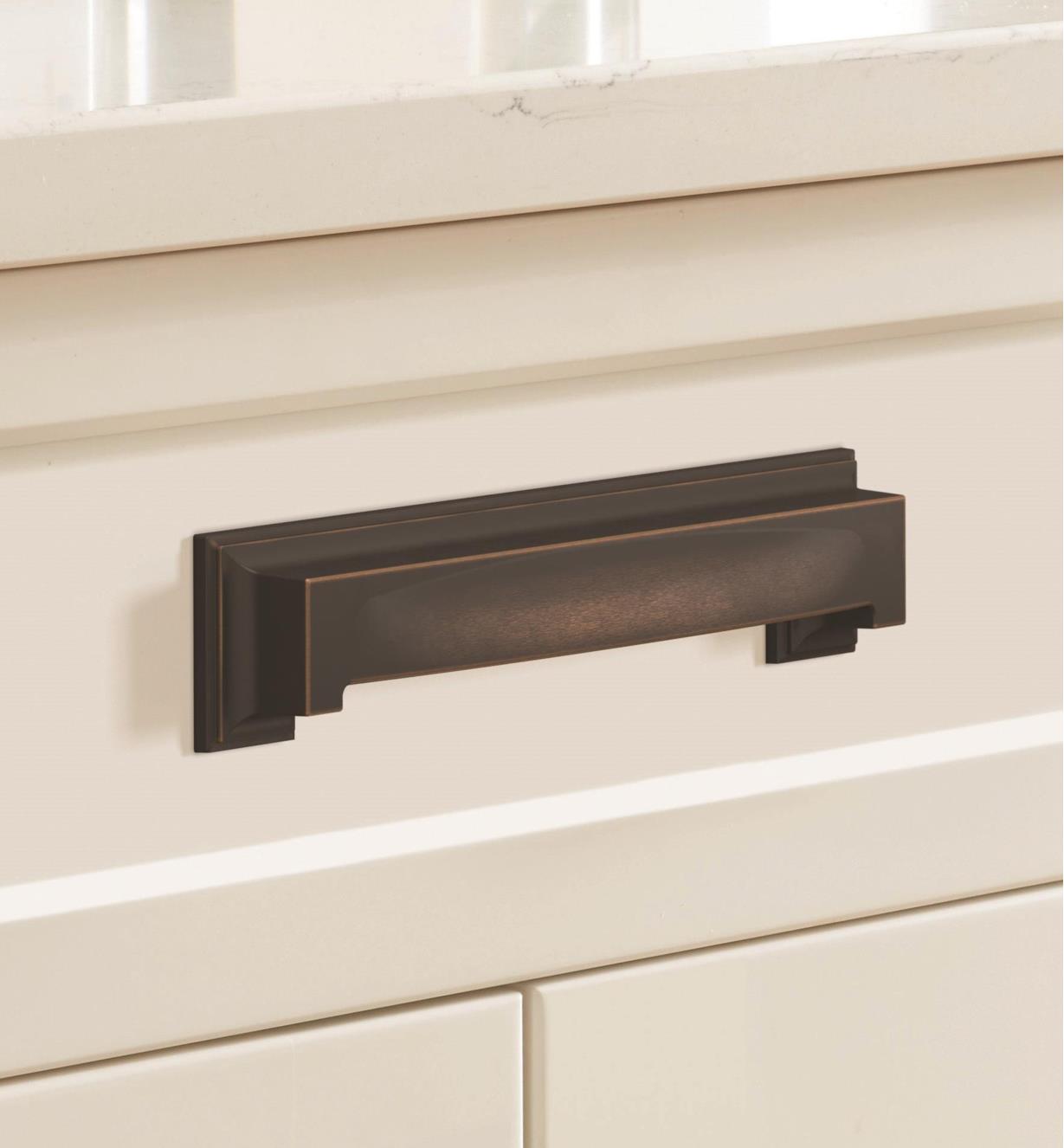 An oil-rubbed bronze Appoint cup pull connected horizontally to a white drawer
