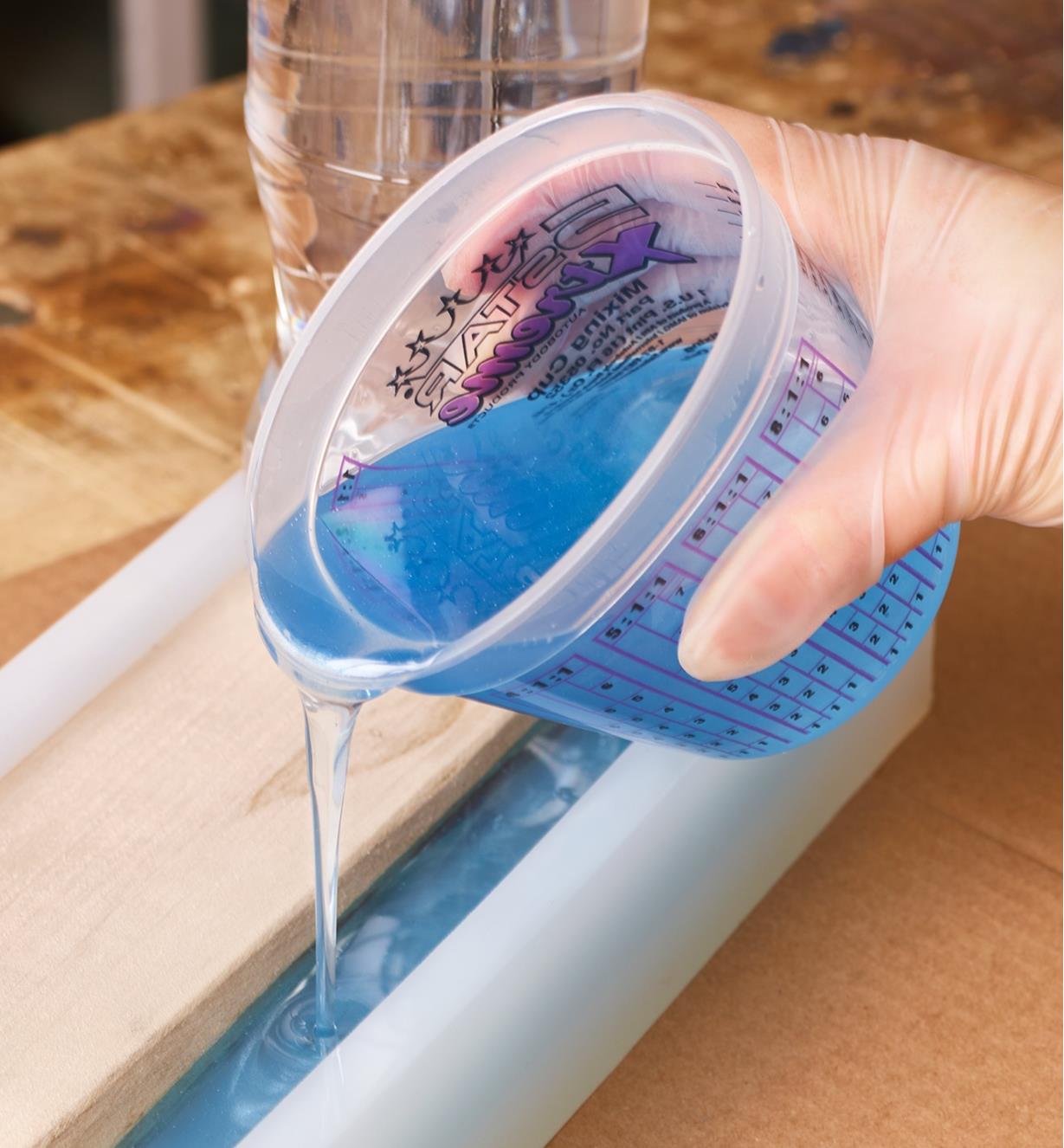Pouring blue epoxy from a measuring and mixing cup while squeezing the sides to form a spout
