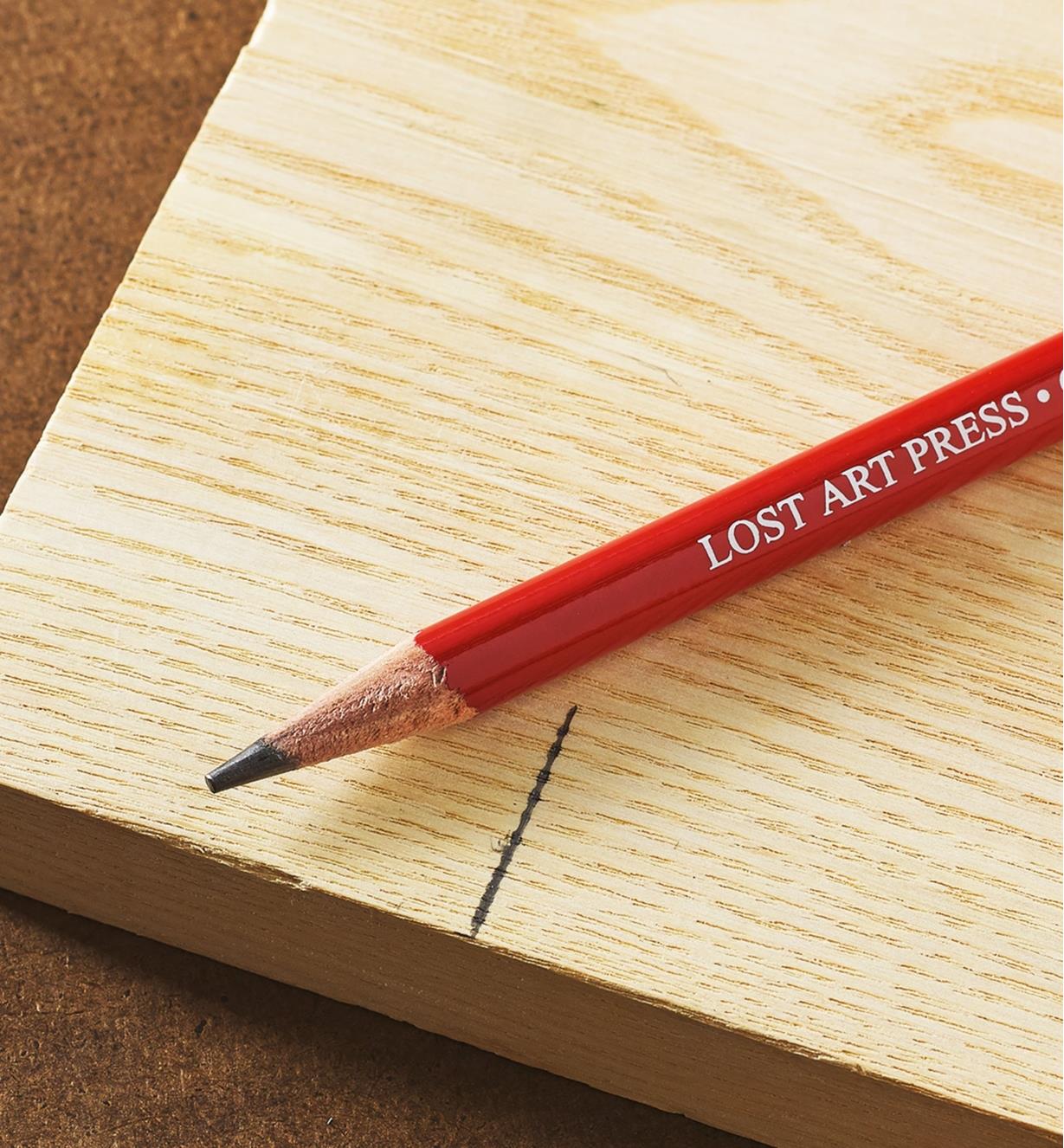 A Lost Art Press woodworking pencil on a piece of wood next to a dark pencil mark