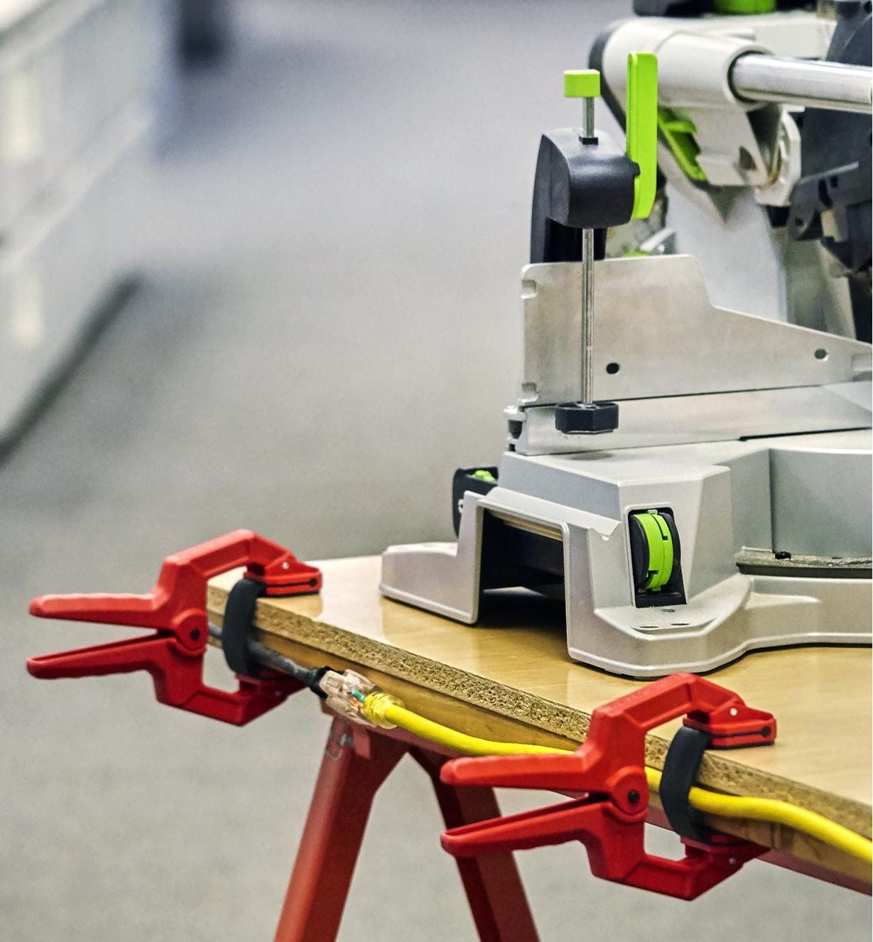 Two edging clamps being used to keep a power cord in place along the edge of a miter-saw stand