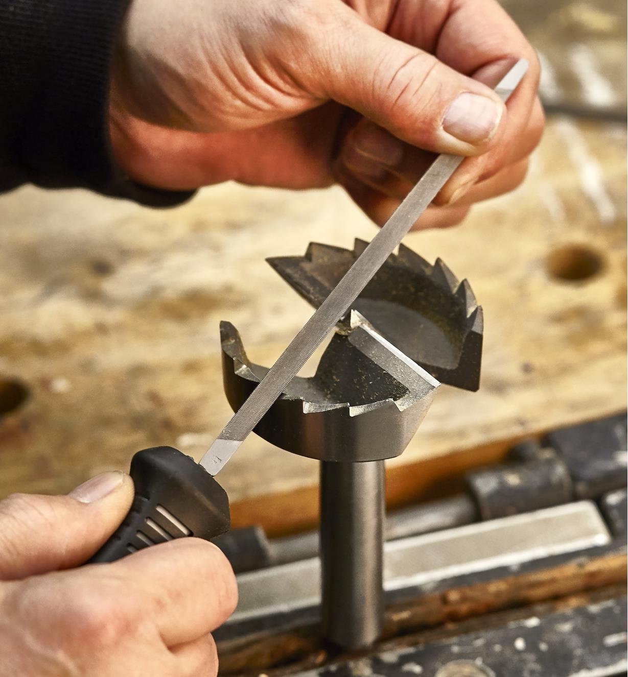 A woodworker uses a triangular slim file to sharpen a saw-tooth drill bit