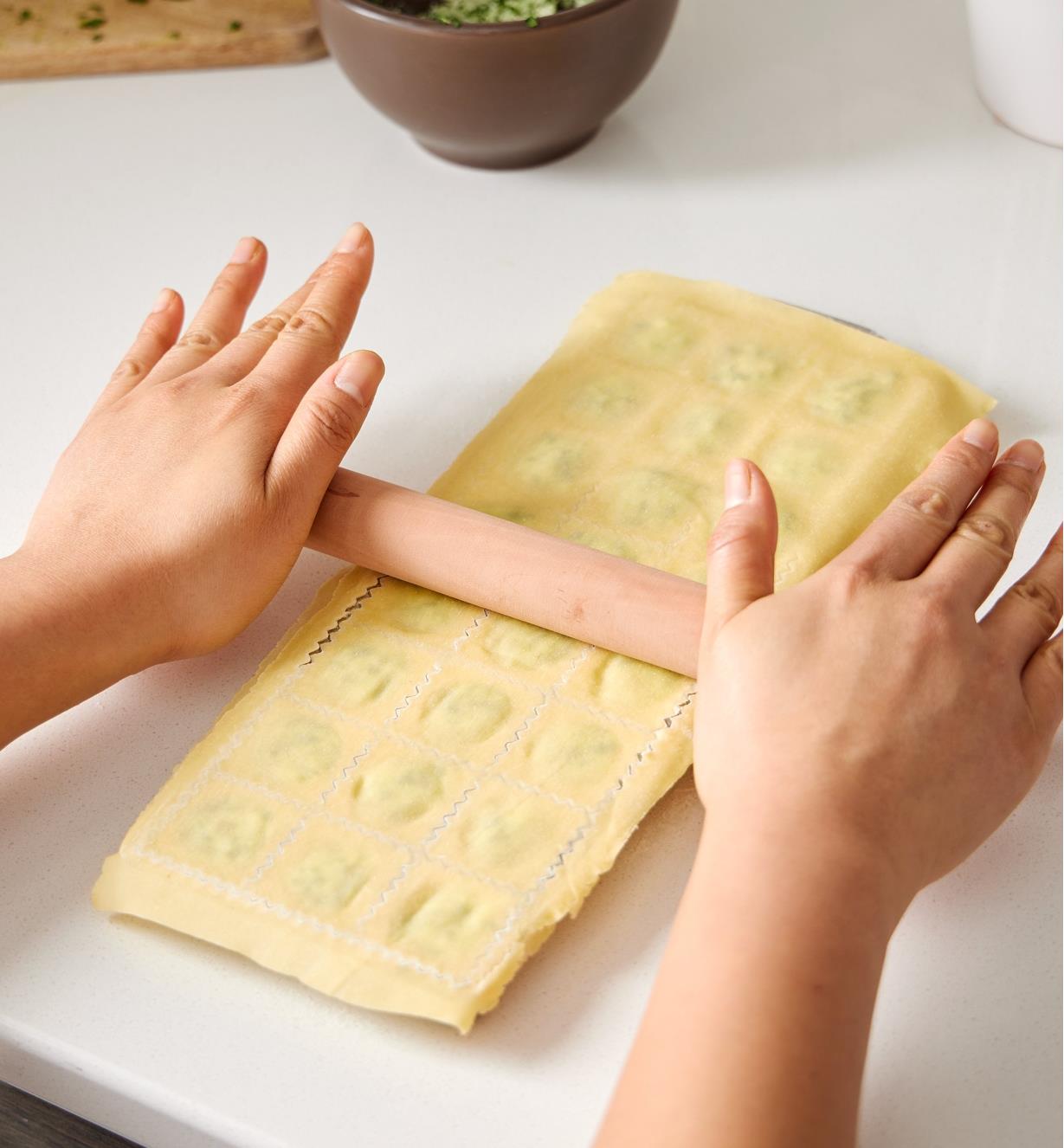 Passing the roller over the pasta-covered ravioli mold to seal the layers