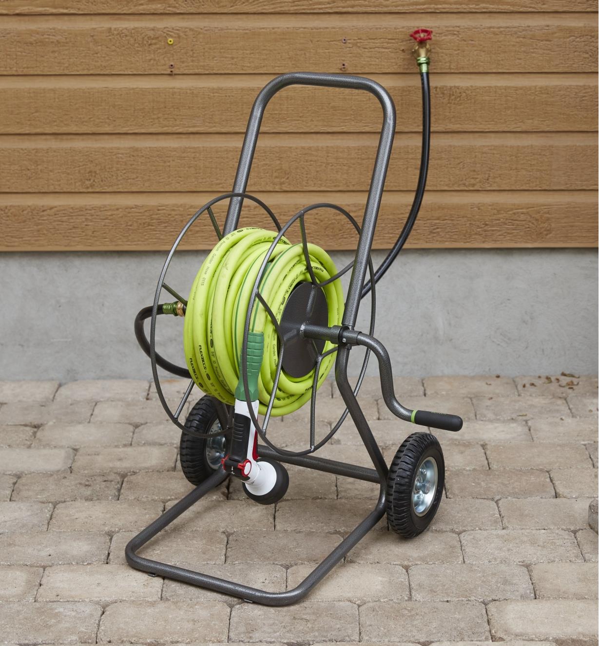 Hose reel cart holding garden hose with a sprayer on a patio