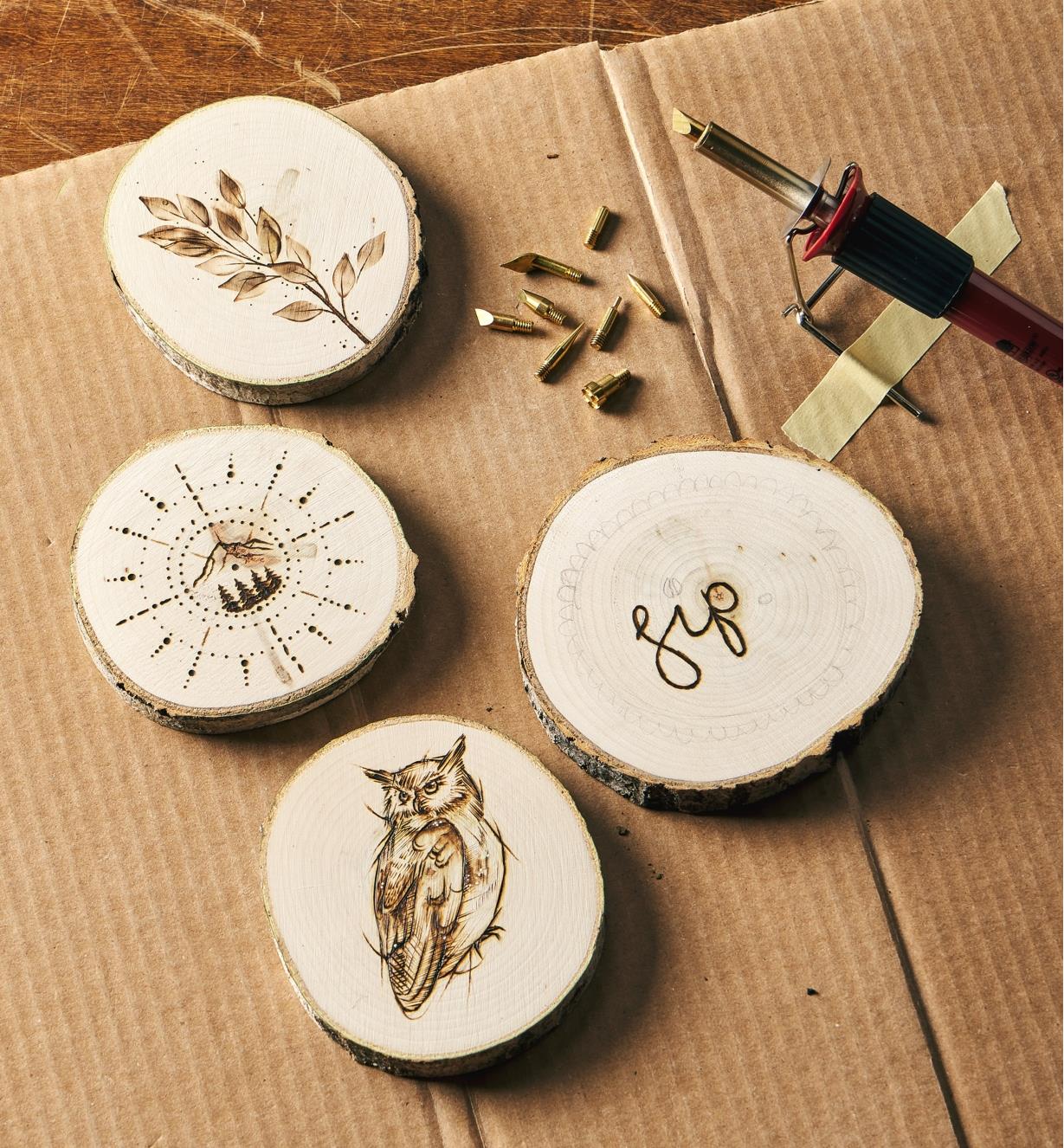 Four aspen rounds adorned with wood-burned designs next to the heat pen and interchangeable nibs