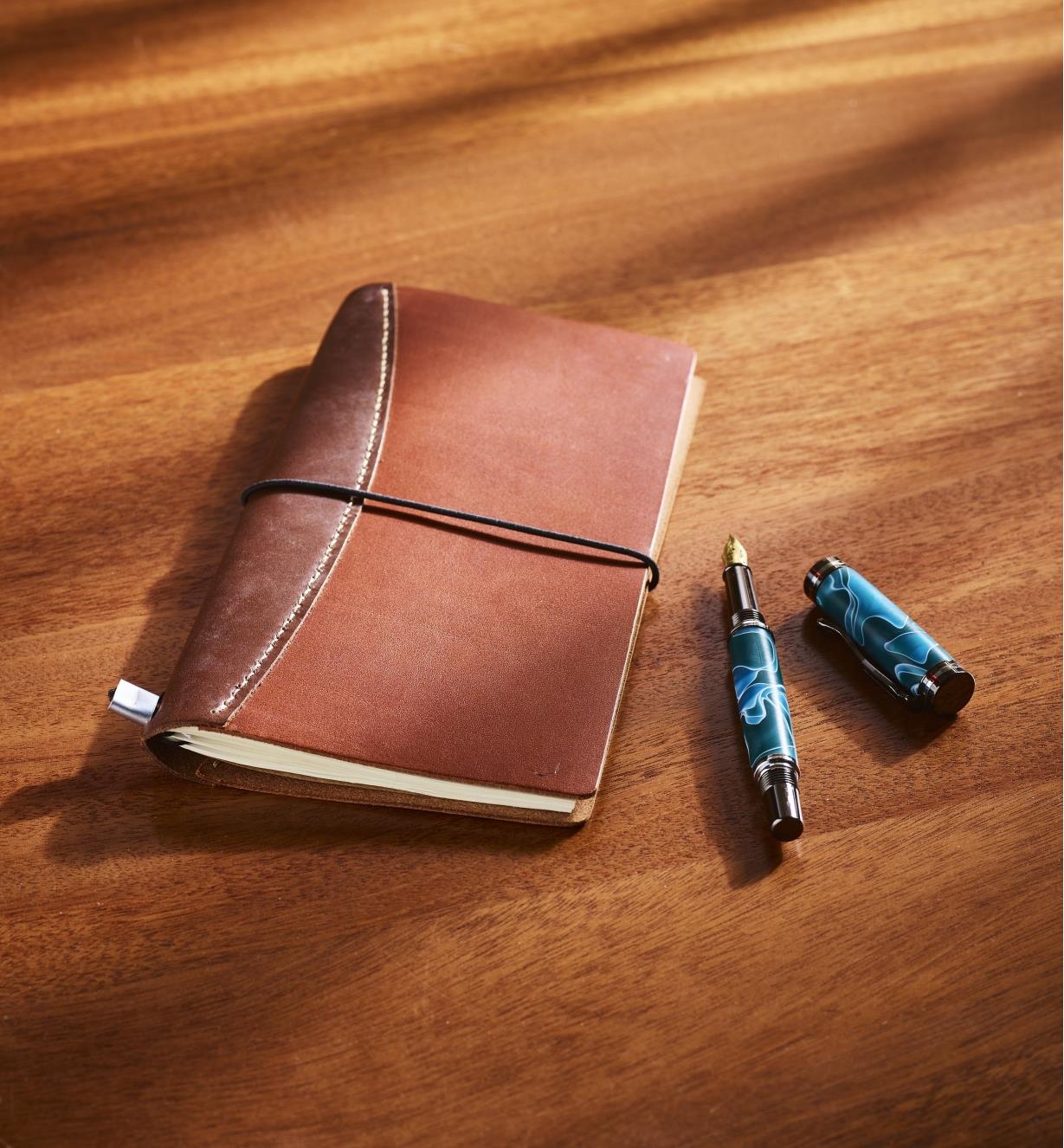 A completed leathercraft notebook sits next to a calligraphy pen