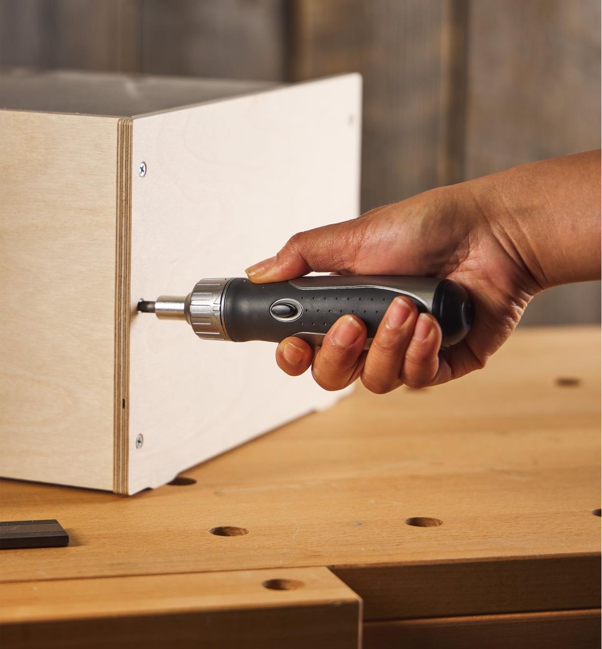 A ratcheting screwdriver being used to tighten a screw on a wooden box