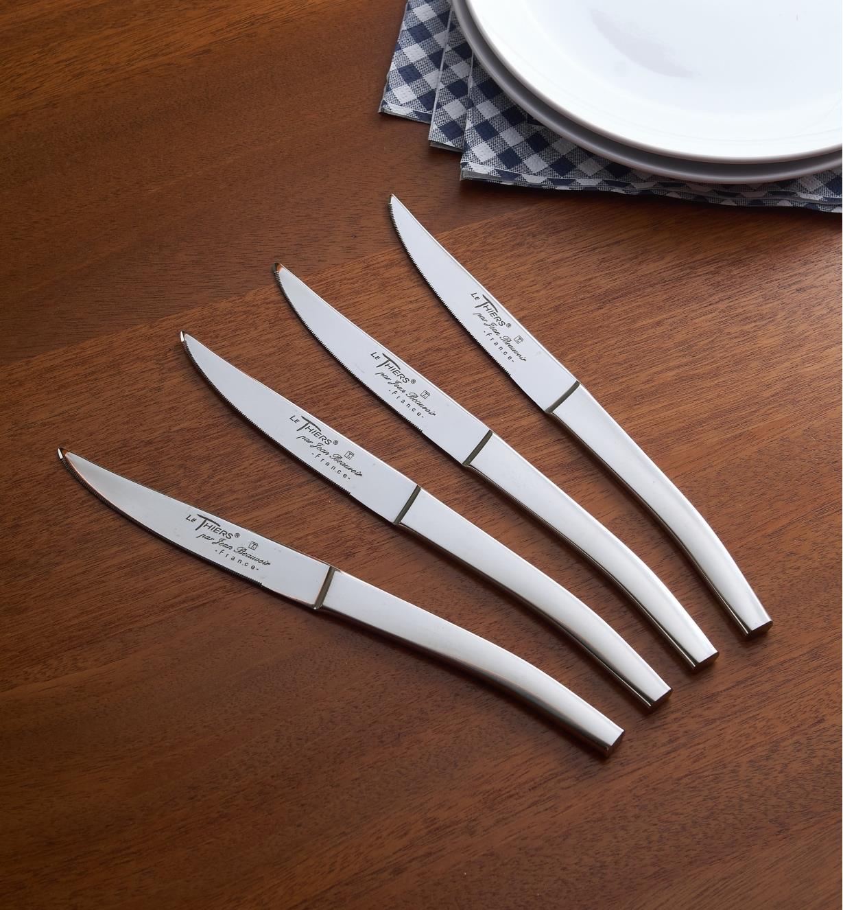 Quatre couteaux de bistro Le Thiers déposés sur une table à manger près d’une pile d’assiettes et de serviettes de table