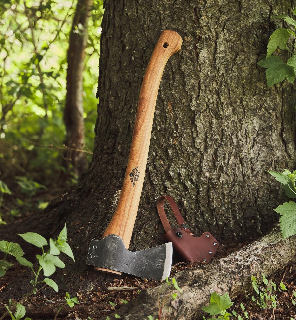 A Gränsfors small forest axe leaning against the trunk of a tree, next to its leather case