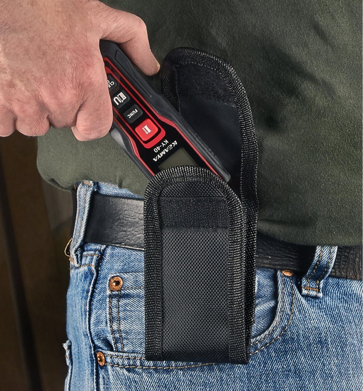 A pocket laser measure is being slid into a belt holster