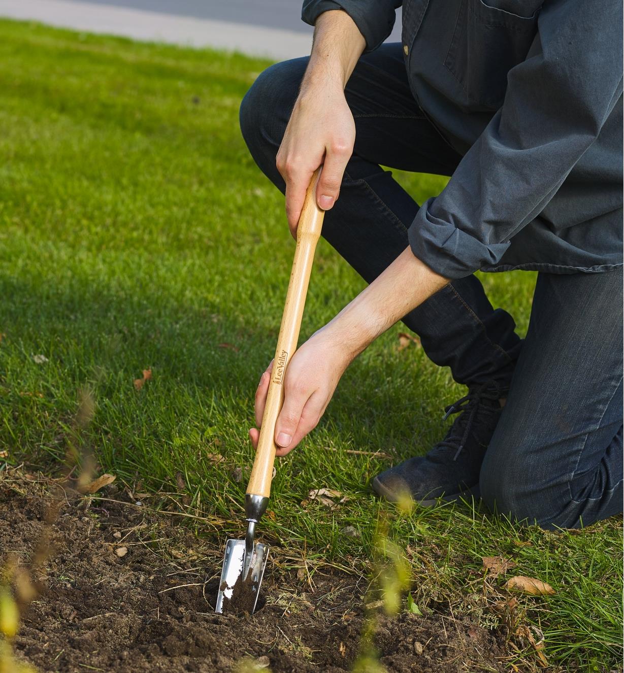 Personne creusant un trou dans le jardin avec un plantoir à bulbes à manche mi-long