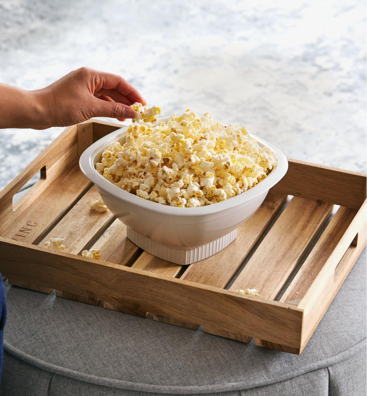 A popper full of popcorn on a wooden tray