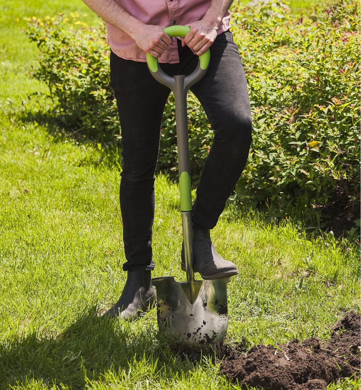 A person using an ergonomic shovel to dig in a lawn