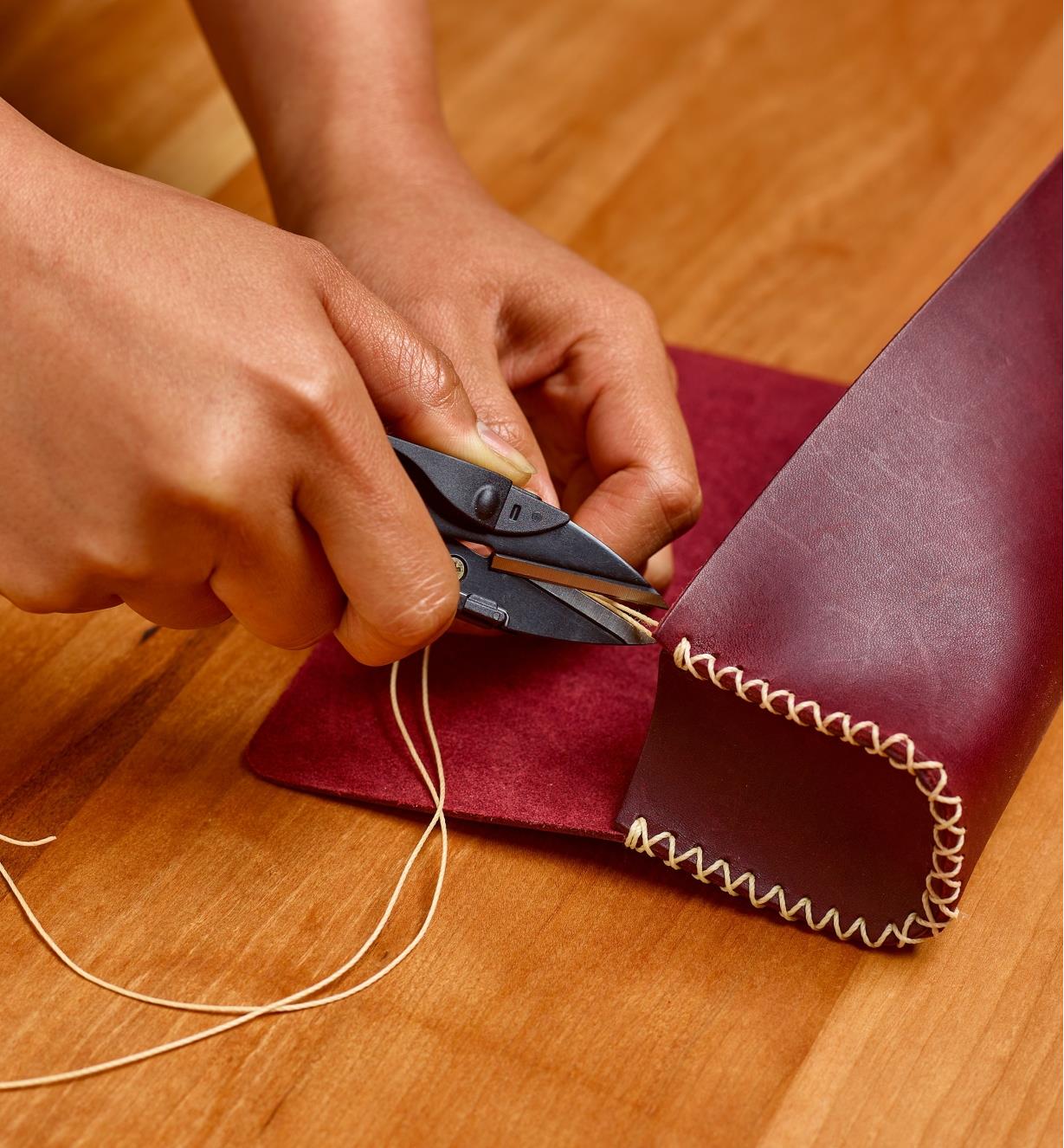 Using micro shears to trim a waxed linen thread on a leatherworking project
