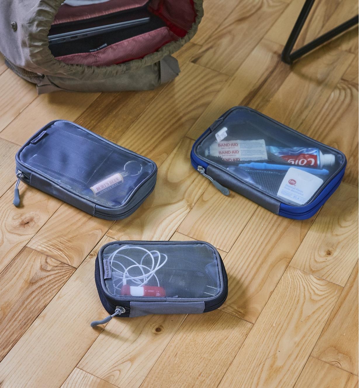 Trois pochettes de voyage près d’un grand sac à dos sur un plancher