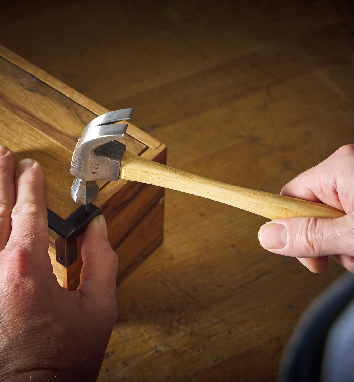 Holding a wooden box steady as a hammer drives a small nail to attach a box corner