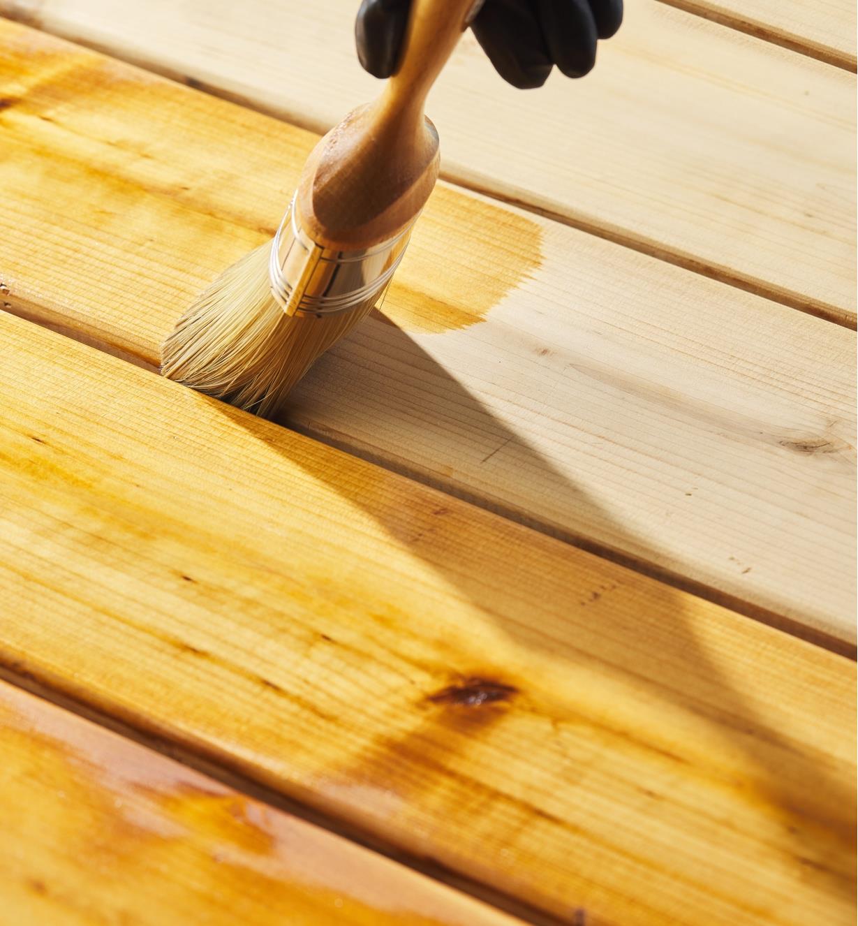 Using a brush to apply Osmo clear decking oil to a wooden deck