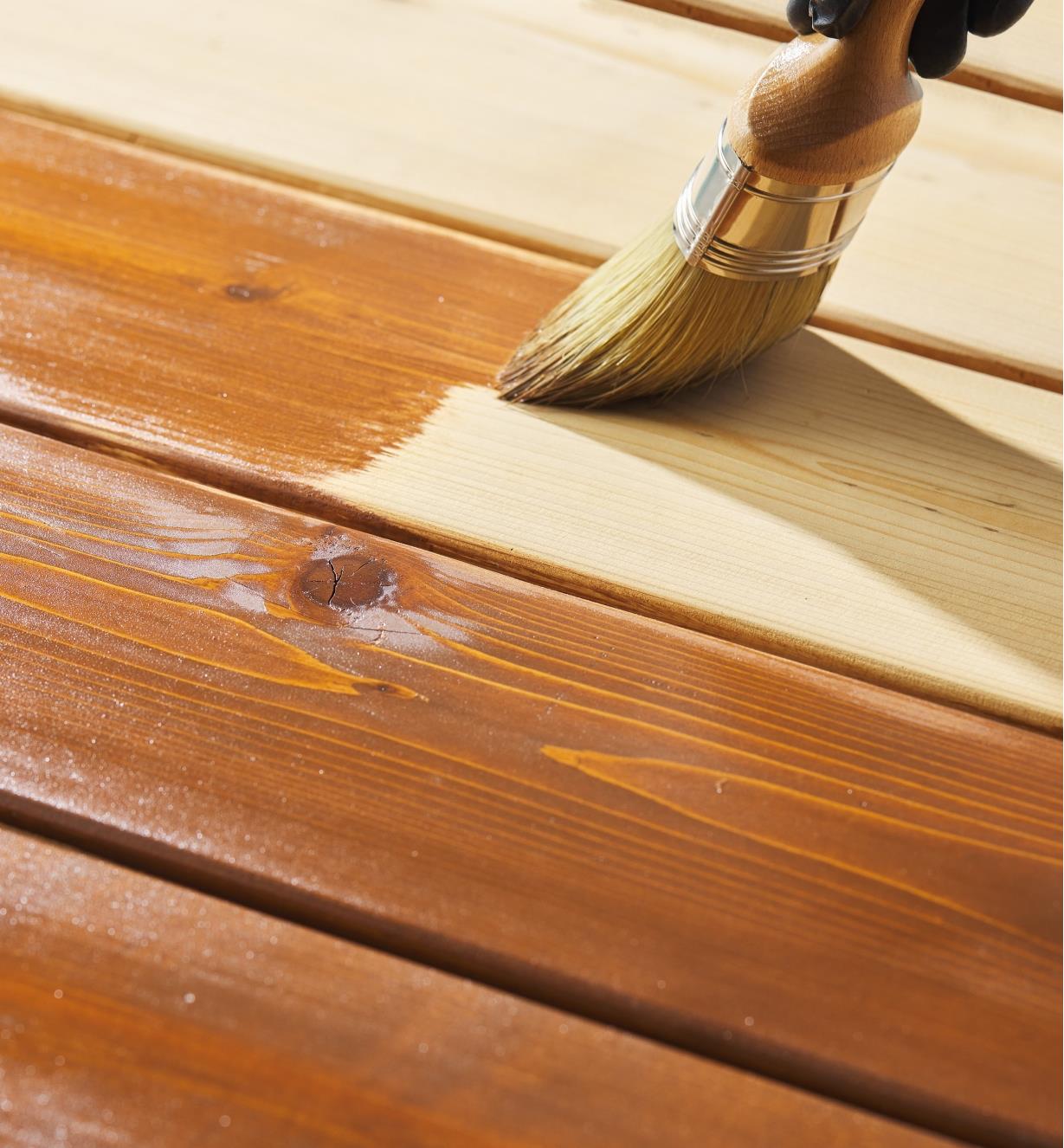 Using a brush to apply Osmo thermowood decking oil to a wooden deck
