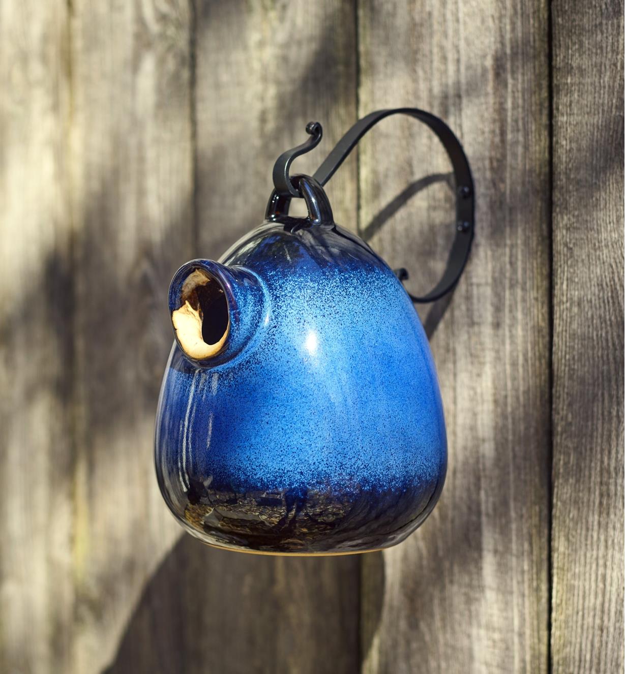 The ceramic bird home suspended from a hanger mounted on a wall
