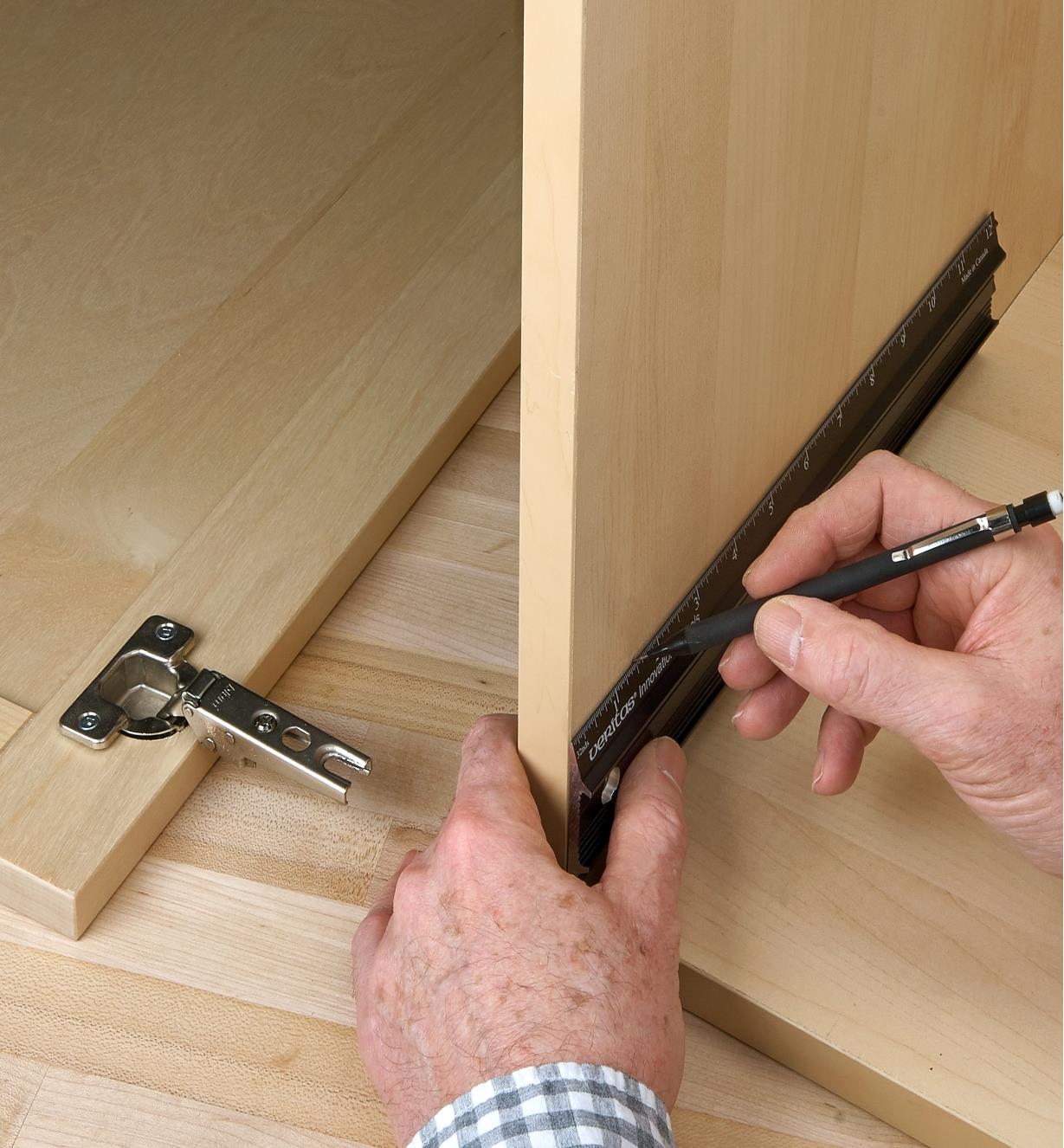 Using a pencil and a 12”/300mm shop rule to mark hinge locations on an inside cabinet wall